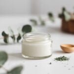 Ein Glas mit selbstgemachter Eukalyptus-Menthol-Salbe, umgeben von frischen Eukalyptusblättern und einem Holzlöffel – ein natürliches Hausmittel gegen Erkältung.