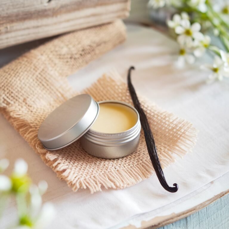Metall-Dose mit natürlichem, vanilleduftendem Lippenbalsam auf Jutestoff, umgeben von getrockneten Vanilleschoten für eine rustikale Optik. Ideal für Themen rund um DIY-Beauty oder natürliche Hautpflege.